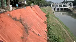 Warga melintasi lokasi tanah longsor yang ditutupi terpal besar di pinggir Kanal Banjir Timur, Jakarta, Kamis (18/6/2020). Warga setempat mengaku khawatir terjadi longsor susulan karena terpal dan karung pasir yang digunakan untuk menutupi lokasi longsor kian rapuh. (merdeka.com/Iqbal S. Nugroho)