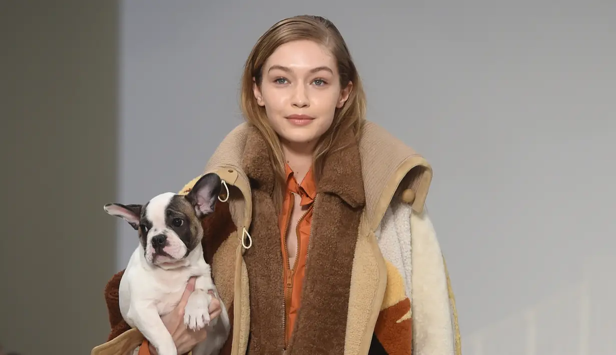 Model asal AS, Gigi Hadid menggendong anak anjing saat memamerkan rancangan Tod's di Milan Fashion Week, Milan, Italia, Jumat (23/2). (Filippo MONTEFORTE/AFP)
