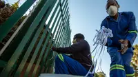 Silva Cossa dan Leonard Makuya, dua orang pengurus, mengikat pita ke pagar gereja St James Presbyterian di Bedford Gardens, Johannesburg, Rabu (29/7/2020). Pita tersebut mewakili warga Afrika Selatan yang meninggal akibat virus corona COVID-19. (AP Photo/Themba Hadebe)