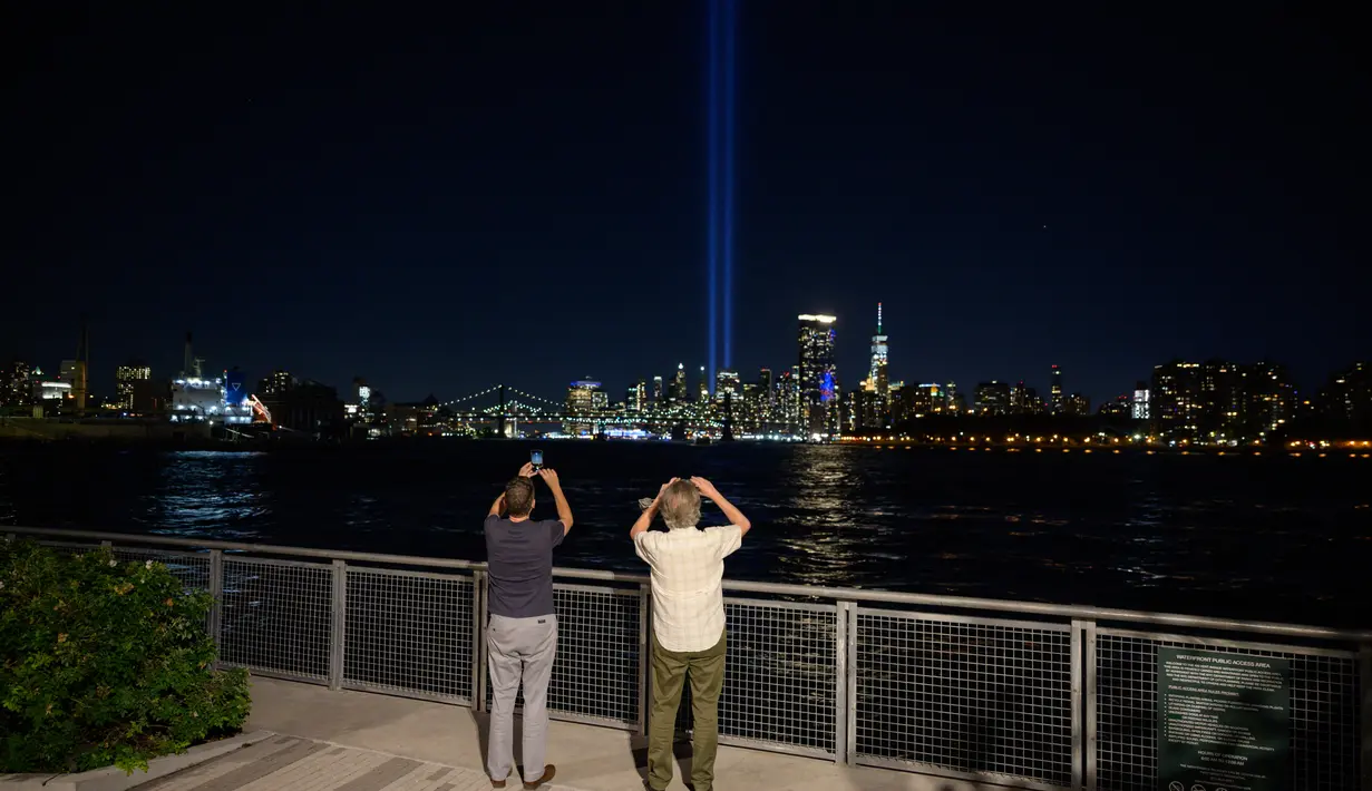 Orang-orang mengambil foto dari instalasi 'Tribute in Light' di tepi perairan Brooklyn untuk memperingati serangan teroris 9/11, di New York (10/9/2021). (AFP/Ed Jones)