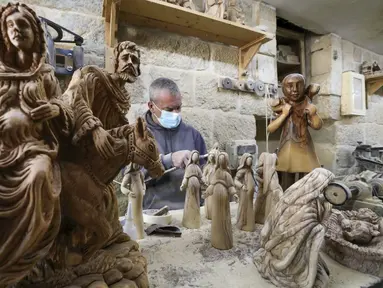 Seorang tukang kayu Palestina mengukir patung keagamaan dari kayu zaitun di sebuah toko dekat Church of the Nativity, Betlehem, Tepi Barat, 21 Desember 2020. Bahan dasar pembuatan patung tersebut menggunakan kayu zaitun. (HAZEM BADER/AFP)