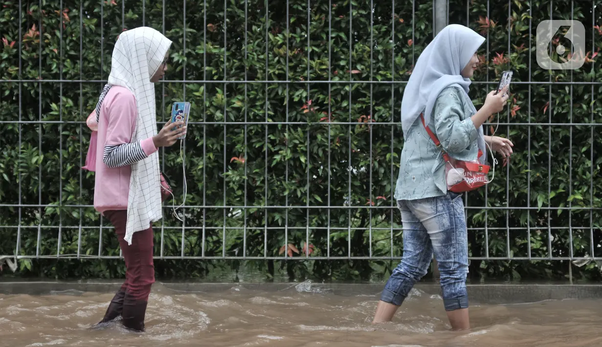 Warga pengguna transportasi umum berjalan kaki melintasi banjir di Jalan Ahmad Yani, Jakarta, Minggu (23/2/2020). Pengguna transportasi umum seperti Transjakarta dan ojek online terpaksa berjalan kaki akibat kendaraan yang mereka tumpangi tidak bisa melintasi banjir. (merdeka.com/Iqbal S. Nugroho)