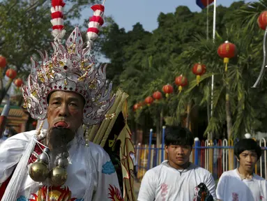 Seorang pria mengenakan kostum unik dengan kail tajam yang menembus pipinya dalam acara Hei Neak Ta atau parade roh untuk memperingati Cap Go Meh, Kamboja, (21/2). Cap Go Meh merupakan rangkaian acara dari tahun baru Imlek. (REUTERS/Samrang Pring) 	