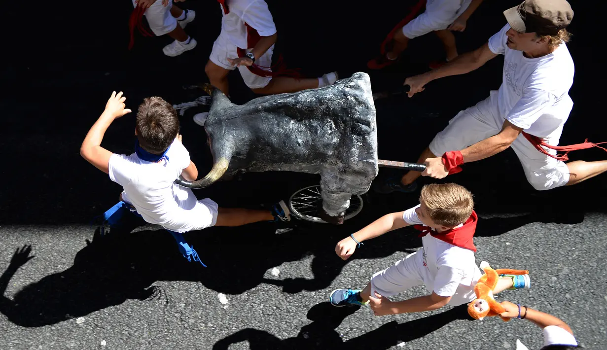 Seorang pria mendorong banteng mainan untuk mengejar anak-anak saat Encierro Txiki selama Festival San Fermin di Pamplona, Spanyol (13/7). Karena menggunakan banteng mainan anak-anak akan aman dari cedera. (AFP Photo/Ander Gillenea)