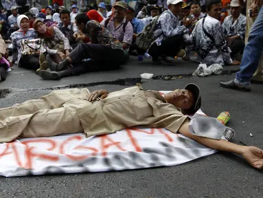 Seorang guru terlihat tidur di tengah jalan karena lelah usai melakukan unjuk rasa di depan Gedung DPR/MPR, Jakarta, Selasa (15/9/2015). Ribuan guru honorer melakukan aksi demo menuntut perubahan status honorer K2 menjadi PNS. (Liputan6.com/Yoppy Renato)