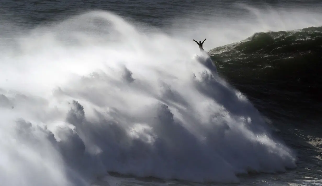 Peselancar mengangkat tangannya saat keluar dari ombak selama sesi selancar derek di Praia do Norte di Nazare, Portugal (29/10/2020). Gelombang besar muncul oleh Badai Epsilon di Atlantik Utara, mencapai pantai barat Portugis menarik peselancar ombak besar ke Nazare. (AP Photo/Pedro Rocha)