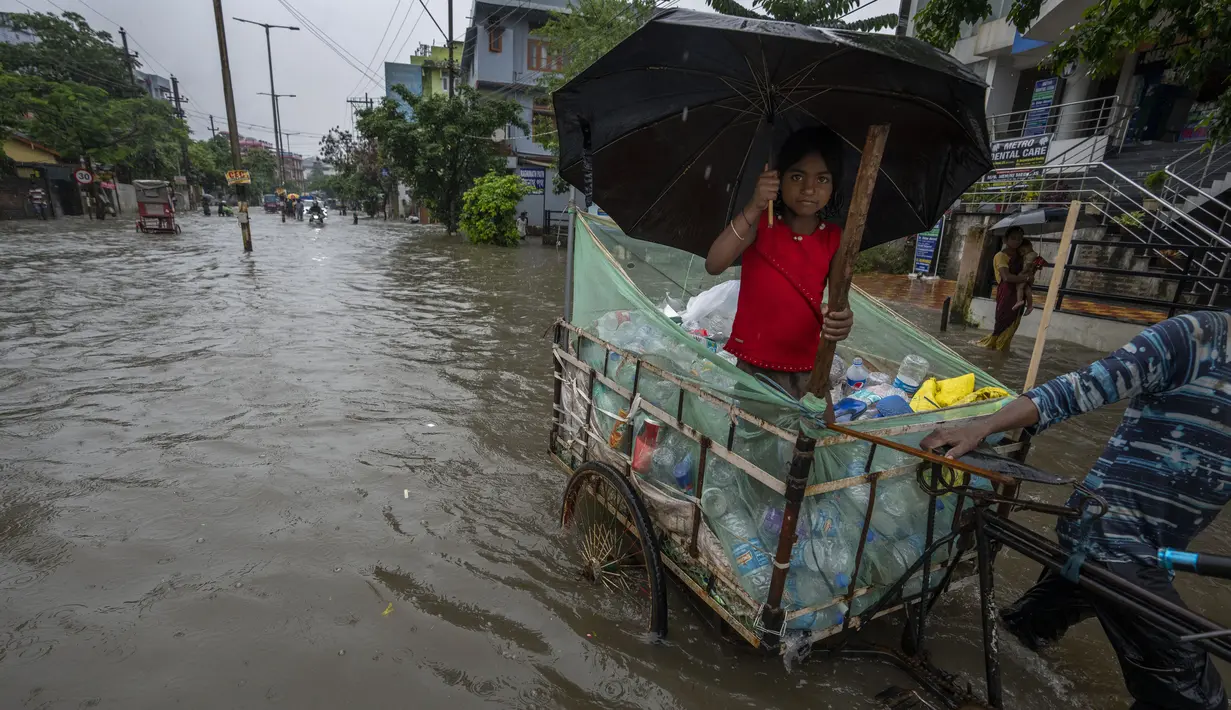 Seorang gadis memegang payung dan berjalan di atas gerobak melalui jalan yang banjir saat hujan deras di Guwahati, negara bagian Assam, India, Kamis (16/6/2022). (AP Photo/Anupam Nath)