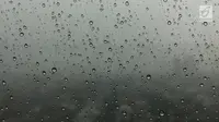 Tetesan air hujan yang ada di jendela kaca dengan latar belakang mendung menyelimuti langit Jakarta, Kamis (1/2). BMKG juga meminta warga mengantisipasi potensi angin berkecepatan tinggi. (Liputan6.com/Immanuel Antonius)