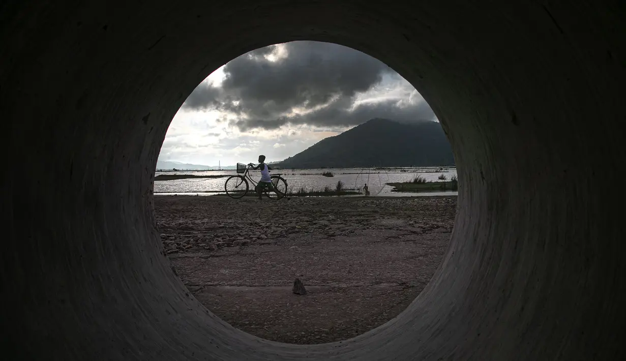 Seorang bocah lelaki India mendorong sepedanya saat seorang nelayan meletakkan jaringnya di air banjir yang surut di pinggiran Gauhati, India, Senin (14/9/2020). (AP Photo / Anupam Nath)