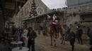 Issa Kassissieh, berpakaian seperti Sinterklas melakukan tur menaiki unta menjelang liburan Natal mendatang, di Kota Tua Yerusalem, Kamis (23/12/2021). Dia mencoba memberikan keceriaan liburan dengan menawarkan pohon Natal gratis kepada para penduduk. (AP Photo/Oded Balilty)