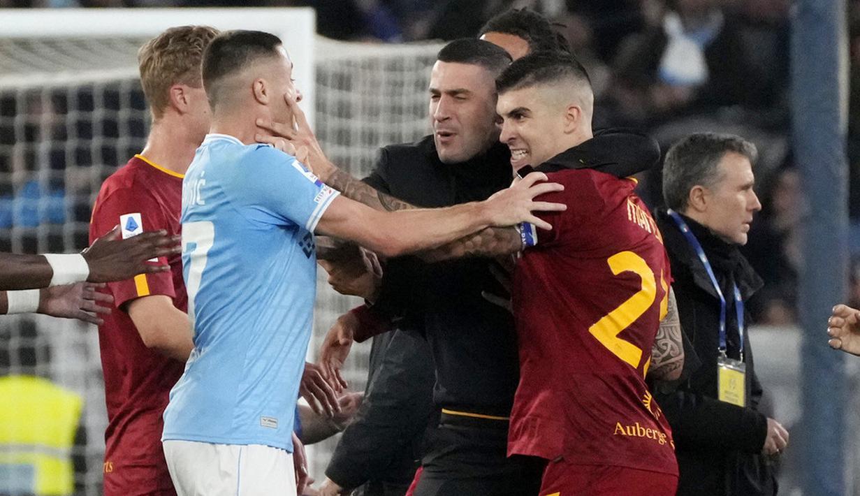 Pemain Lazio, Adam Marusic, bersitegang dengan pemain  AS Roma, Gianluca Mancini, pada laga pekan ke-27 Serie A 2022/2023 di Stadion Olimpico, Senin (20/03/2023). Total ada tiga kartu merah dikeluarkan wasit di laga panas ini. (AP Photo/Gregorio Borgia)