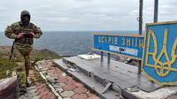 Seorang tentara Ukraina berjalan melewati tanda "Pulau Ular, milik kita" di Pulau Ular, Laut Hitam, Ukraina, 18 Desember 2022. Pasukan Rusia menduduki pulau itu pada awal-awal invasinya ke Ukraina, namun akhirnya mundur beberapa bulan kemudian. (AP Photo/Michael Shtekel)