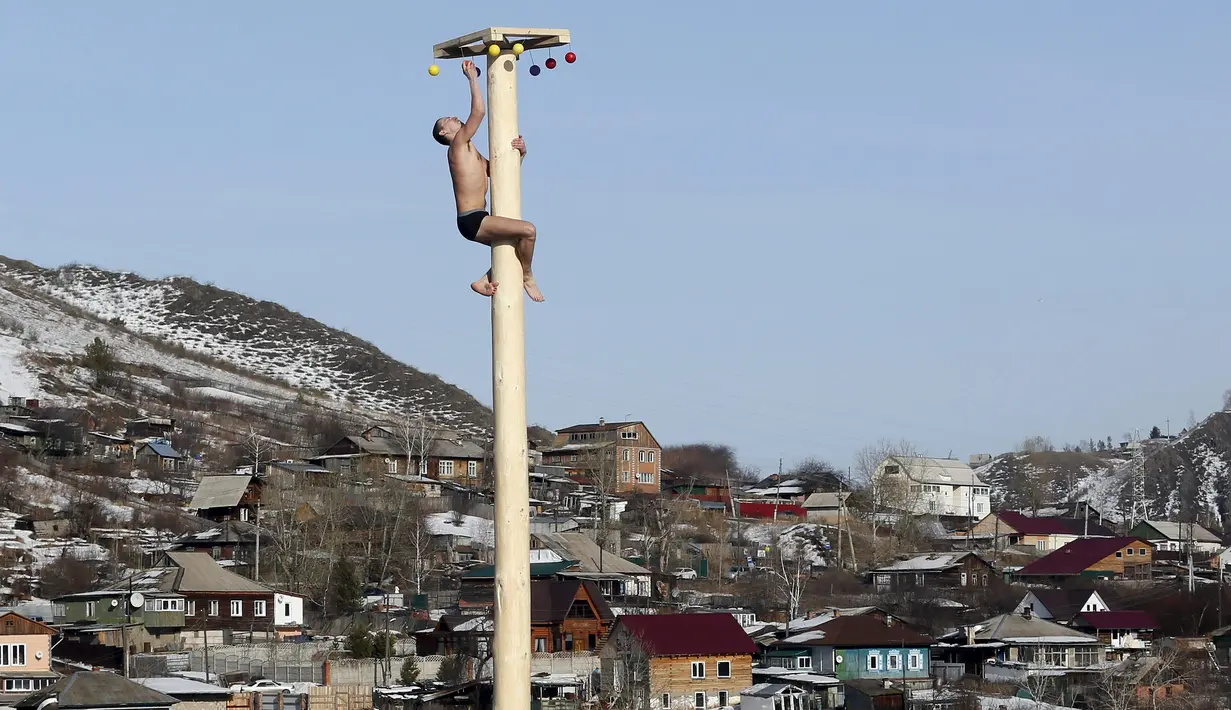Seorang pria memanjat tiang kayu yang tinggi untuk mendapatkan hadiah selama perayaan Maslenitsa di kota Krasnoyarsk, Rusia, (13/3). perayaan Maslenitsa adalah kegiatan untuk menandai berakhirnya musim dingin di Rusia. (REUTERS / Ilya Naymushin)