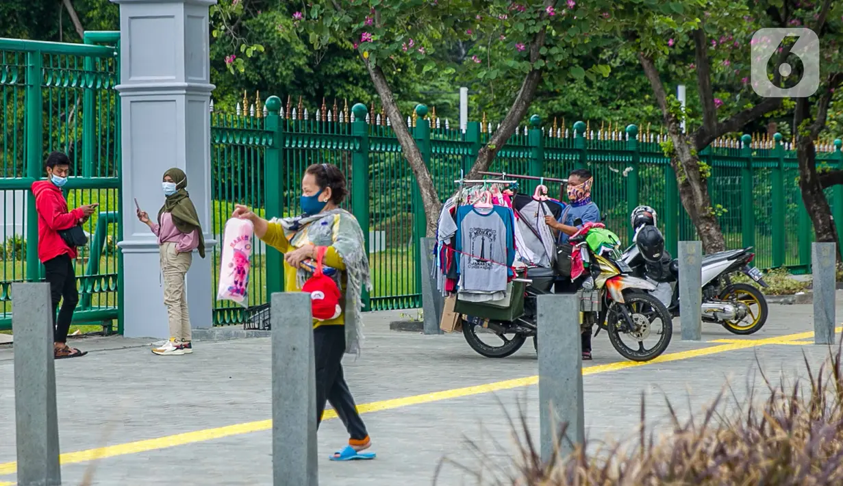 Pedagang kaos cendera mata keliling mencoba peruntungan dari para pengunjung yang ingin menyaksikan Tugu Monas Jakarta dari balik pagar, Sabtu (2/1/2021). (Liputan6.com/Faizal Fanani)