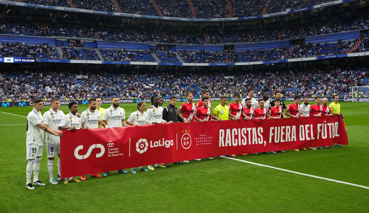 Sejumlah pemain Real Madrid membentangkan banner yang bertuliskan "Rasis, di luar sepak bola" pada laga lanjutan Liga Spanyol 2022/2023 antara Real Madrid melawan Rayo Vallecano pada Kamis (25/05/2023) dini hari WIB. Los Blancos memberikan aksi solidaritas sebelum laga tersebut setelah Vinicius Jr menjadi korban rasisme pada Minggu (21/05/2023) lalu. (AP Photo/Manu Fernandez)