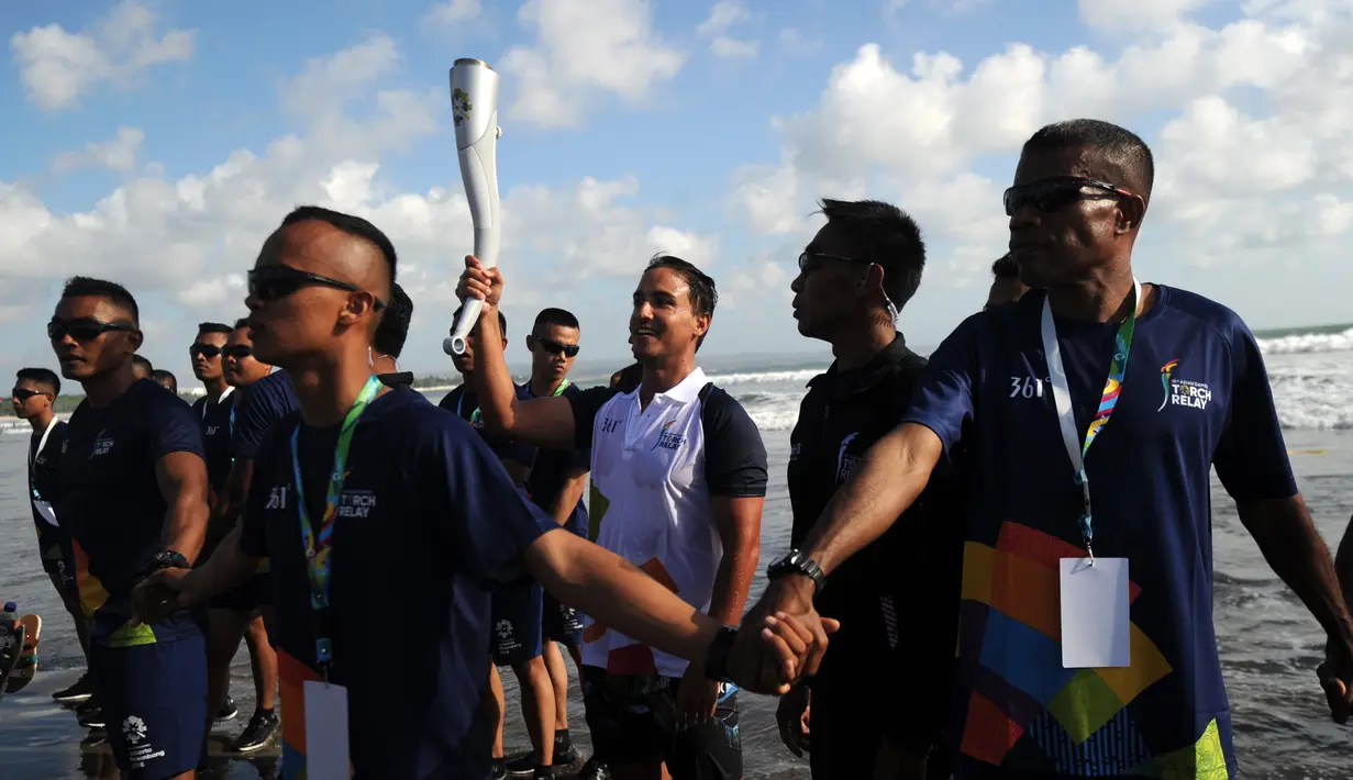 Aktor Hamish Daud (tengah) membawa obor pada kirab obor Asian Games 2018 di Pantai Kuta, Bali, Senin (23/7). Torch Relay Asian Games 2018 melintasi empat kabupaten di Bali dengan arak-arakan berkeliling di sejumlah obyek wisata. (AFP/SONNY TUMBELAKA)