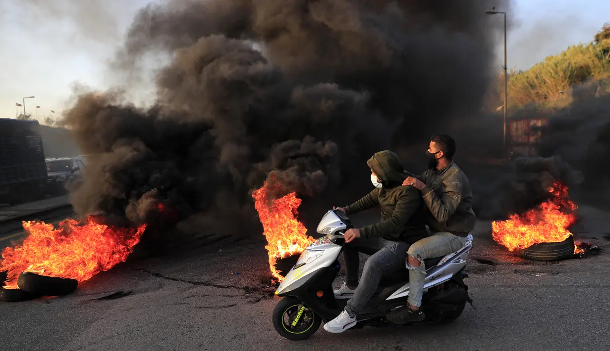 Pengunjuk rasa melewati ban yang dibakar untuk memblokir jalan raya menuju bandara internasional Beirut, Selasa (2/3/2021). Warga Lebanon yang marah memblokir jalan setelah mata uang Lebanon jatuh ke titik terendah baru dalam krisis keuangan yang memicu kemiskinan. (AP Photo/Hussein Malla)