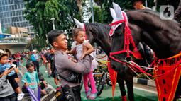 Polisi dari Detasemen Turangga Direktorat Polisi Satwa Polri menaiki seorang anak ke atas kuda saat Car Free Day (CFD) atau Hari Bebas Kendaraan Bermotor di kawasan Bundaran HI, Jakarta, Minggu (19/2/2023).Polisi berkuda selain ditugaskan untuk pengamanan simpatik juga untuk menghibur warga dan anak-anak saat Hari Bebas Kendaraan Bermotor serta memperkenalkan profesi tersebut kepada warga. (Lipitan6.com/Angga Yuniar)