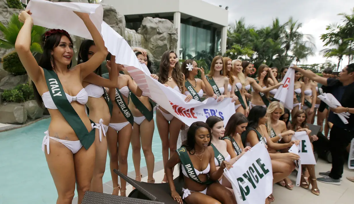 Kontestan Miss Earth 2017, Miss Italia Fabiana Barra (kiri) menggunakan spanduk untuk menutupi dirinya saat hujan mulai turun selama sesi pemotretan dengan bikini di tepi kolam renang hotel di Manila, Filipina, Senin (30/10). (AP/Aaron Favila)