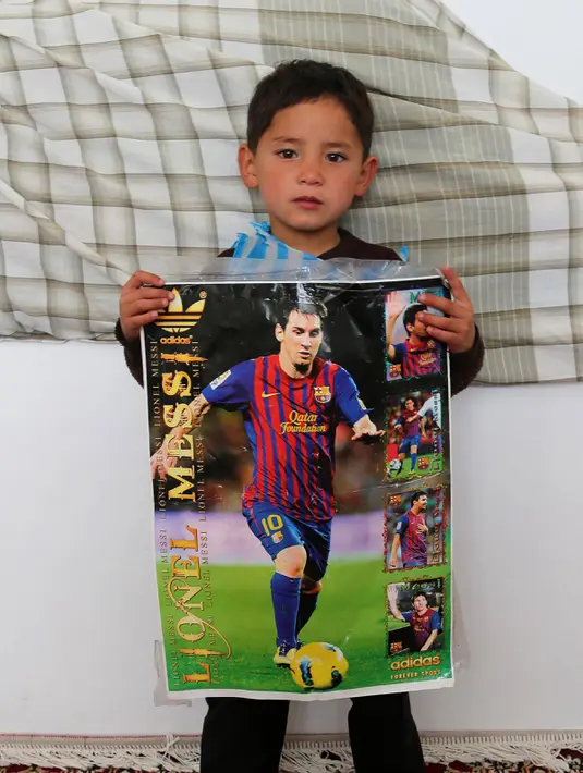 Seorang anak laki-laki Afghanistan, Murtaza Ahmadi, memegang poster Lionel Messi di kabupaten Jaghori, provinsi Ghazni, 29 Januari 2016. Murtaza adalah bocah yang sempat membuat heboh dunia maya karena memakai jersey kantong kresek Messi. (STR/AFP)