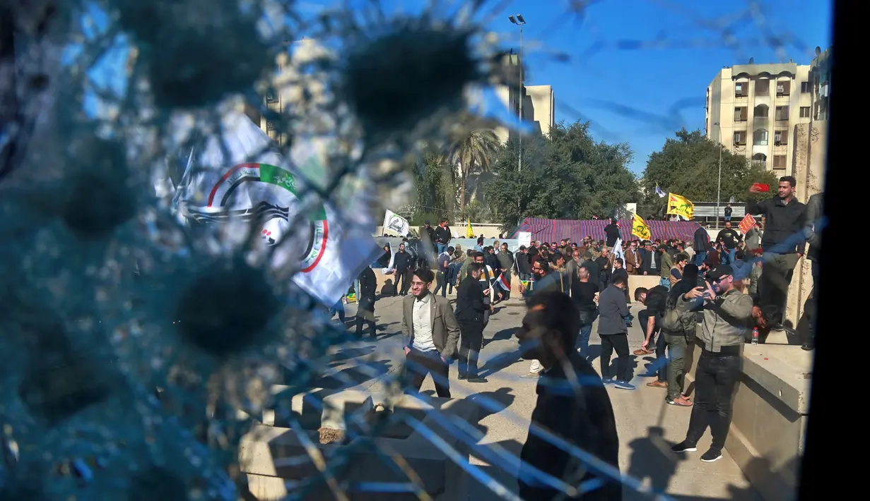 Pendukung milisi Syiah terlihat melalui jendela yang rusak dari sebuah pos pemeriksaan milik kedutaan AS, di depan kedutaan AS, di Baghdad, Irak, Selasa (31/12/2019). (AP Photo/Khalid Mohammed)