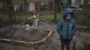 Di halaman rumahnya, Vlad Tanyuk (6) berdiri di dekat makam ibunya Ira Tanyuk, yang meninggal karena kelaparan dan stres akibat perang, di pinggiran Kiv, Ukraina, Senin, 4 April 2022. Gundukan tanah yang ditutupi oleh salib kayu sederhana itu menandai makam ibunya. (AP Photo/Rodrigo Abd)