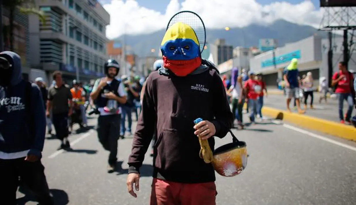Seorang pengunjuk rasa memakai topeng berwarna bendera Venezuela, saat ikut serta dalam demonstrasi anti-pemerintah ke Mahkamah Agung di Caracas, Venezuela, Kamis, 6 Juli 2017. (AP Photo / Ariana Cubillos)