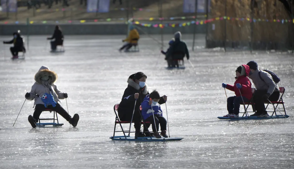 Seorang wanita dan anak-anak mendorong kursi es melintasi kolam beku di taman umum di Beijing, Selasa (17/1/2023). China telah mengumumkan penurunan populasi pertamanya dalam beberapa dasawarsa seiring bertambahnya usia negara terpadat di dunia dan angka kelahirannya yang menurun. (AP Photo/Mark Schiefelbein)