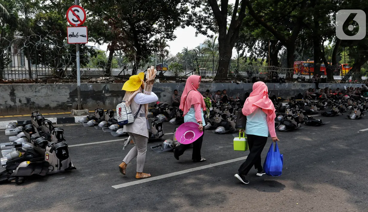 Warga melintasi polisi yang tengah bersiaga di sekitar Gedung DPR RI, Jakarta, Kamis (17/10/2019). Polisi kembali menutup sejumlah ruas jalan menuju kawasan Gedung DPR RI guna menjaga kondusifitas jelang pelantikan Presiden dan Wakil Presiden terpilih. (Liputan6.com/JohanTallo)