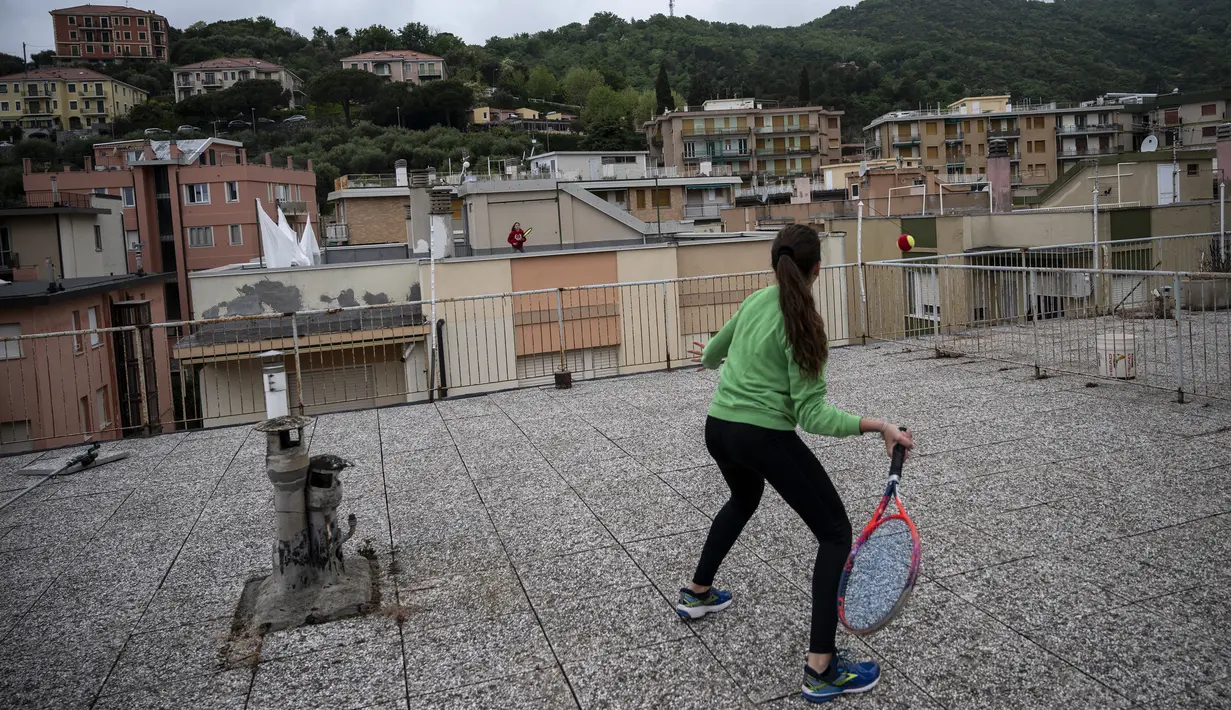 Vittoria Oliveri (depan) bermain tenis dengan Carola di atas atap rumah mereka selama lockdown COVID-19 di Finale Ligure, Wilayah Liguria, Italia (19/4/2020). Setiap hari Carola, 11, dan Vittoria, 13, bermain tenis dari satu atap ke atap lain di rumah mereka untuk berlatih. (AFP/Marco Bertorello)