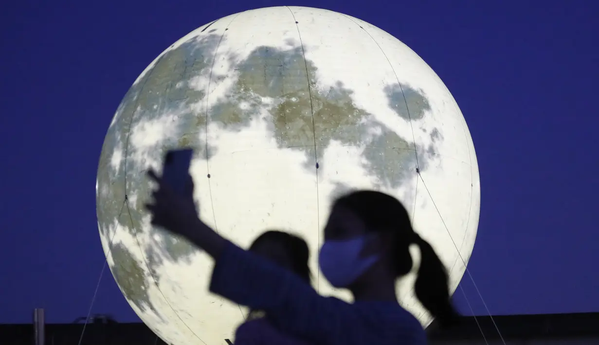 Warga berswafoto dekat instalasi bulan purnama yang bersinar di sebuah taman di Seoul, Korea Selatan, Jumat (18/9/2020). Pejabat setempat memasang bulan purnama buatan untuk meningkatkan semangat saat wabah COVID-19 sekaligus menyambut Chuseok, Thanksgiving versi Korea. (AP Photo/Ahn Young-joon)
