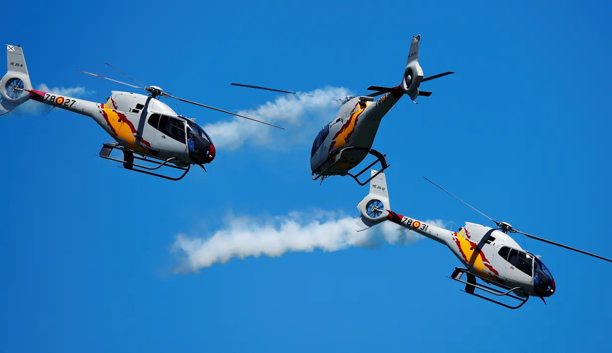 Aksi tim aerobatik Patrulla Aspa bermanuver menggunakan helikopter saat menghebohkan pengunjung di atas Pantai San Lorenzo di Gijon, Spanyol, Minggu (24/7). (REUTERS/Eloy Alonso)