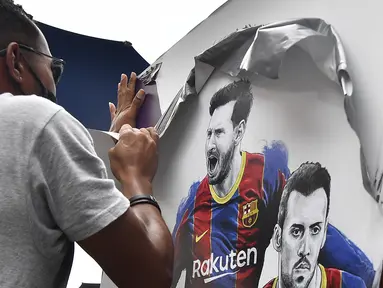 Seorang pekerja melepas poster-poster yang menampilkan pemain depan Barcelona Lionel Messi di stadion Camp Nou di Barcelona (10/8/2021). Prancis menunggu dengan tidak sabar Lionel Messi dengan para pendukung berkumpul di luar lapangan Paris Saint-Germain. (AFP/ Pau Barrena)
