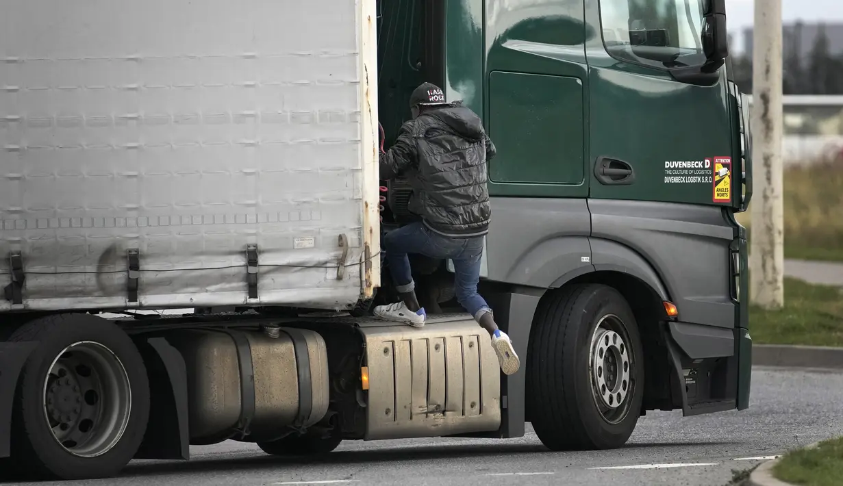 Migran melompati sebuah truk untuk menyeberangi terowongan menuju Inggris di Calais, Prancis pada 14 Oktober 2021. Dalam praktik berbahaya dan berpotensi mematikan, ia mencoba melewati terowongan yang dijaga ketat yang menghubungkan kedua negara dengan bersembunyi di truk. (AP/Christophe Ena)