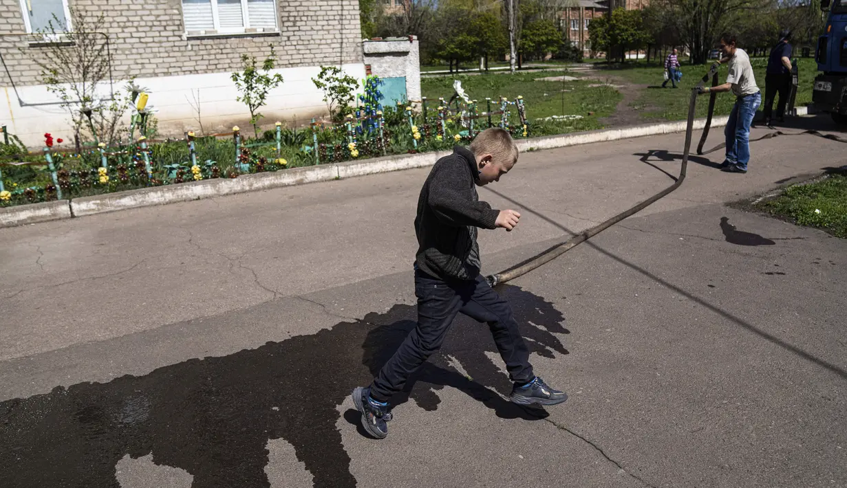 <p>Seorang anak melompati genangan air di Toretsk, Ukraina timur, pada 25 April 2022. Penduduk Toretsk tidak memiliki akses air selama lebih dari dua bulan karena perang Rusia Ukraina. (AP Photo/Evgeniy Maloletka)</p>