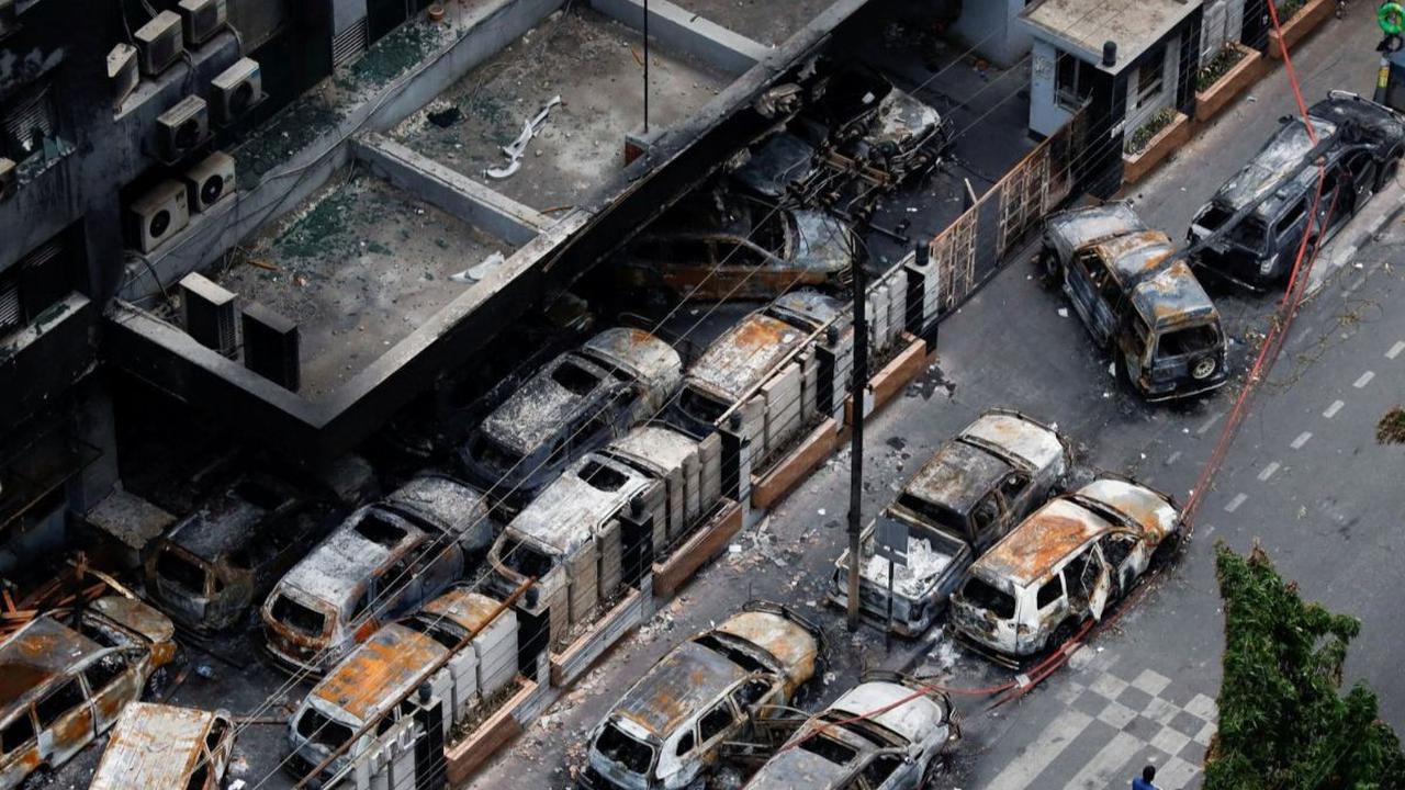 Seorang pria mengendarai becak melewati kendaraan rusak yang dibakar massa dalam aksi unjuk rasa di Dhaka, Bangladesh, pada 21 Juli 2024. Bangladesh dilanda kerusuhan berdarah selama berhari-hari ketika ribuan mahasiswa memprotes aturan baru terkait kuota