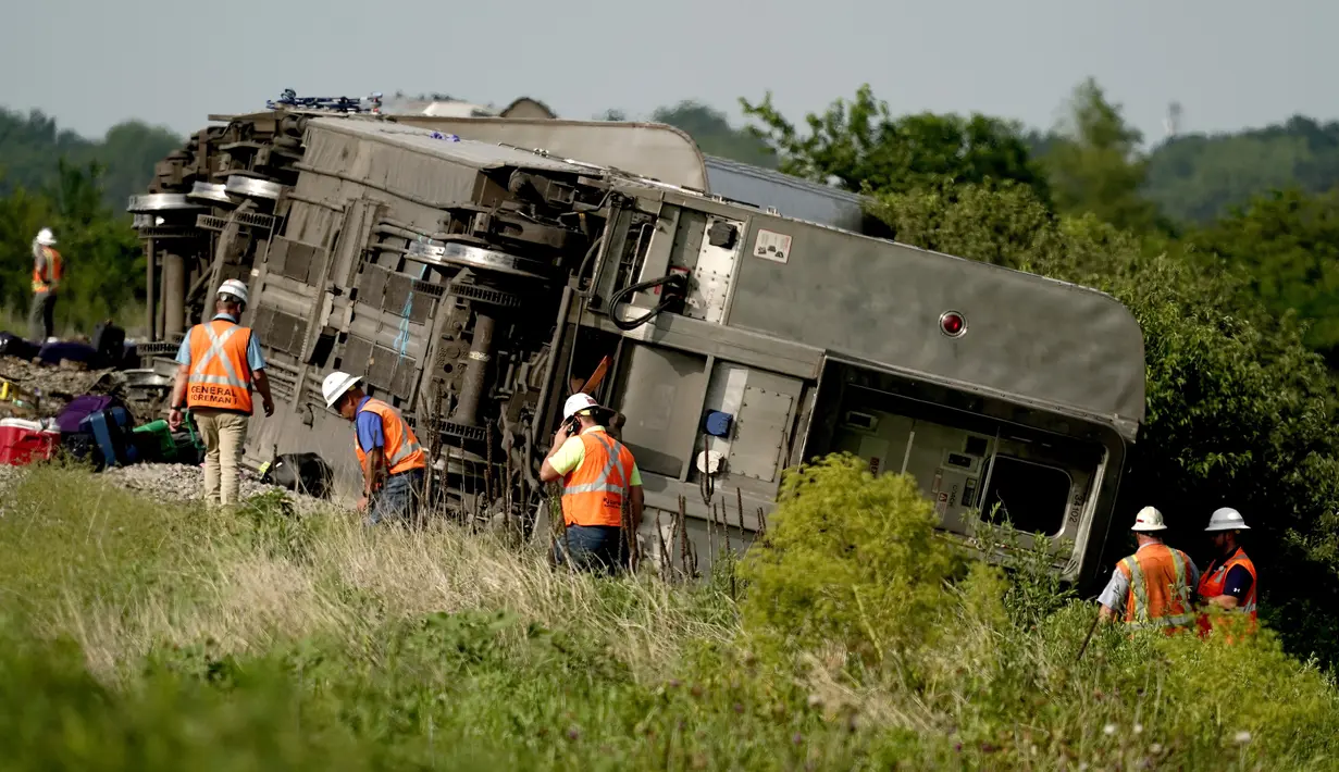 Pekerja memeriksa lokasi kereta Amtrak yang tergelincir setelah menabrak truk sampah di dekat Mendon, Missouri, AS (27/6/2022). Peristiwa itu terjadi sehari setelah kereta lain yang dioperasikan Amtrak bertabrakan dengan kendaraan penumpang di perlintasan kereta api di California, yang mengakibatkan tiga kematian. (AP Photo/Charlie Riedel)