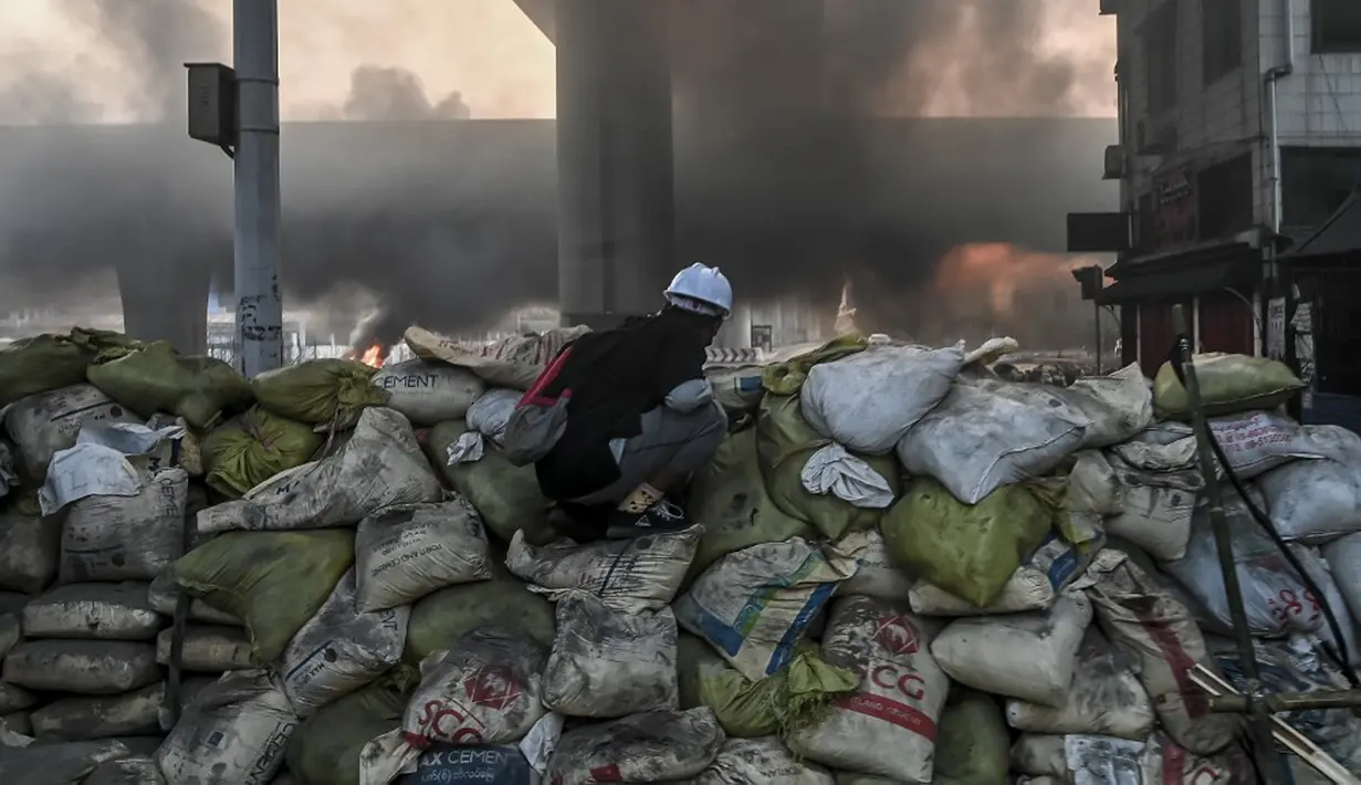 Seorang pengunjuk rasa berlindung di balik barikade darurat yang didirikan untuk menghalangi pasukan keamanan selama demonstrasi menentang kudeta militer di Yangon, Myanmar, 16 Maret 2021. (STR/AFP)