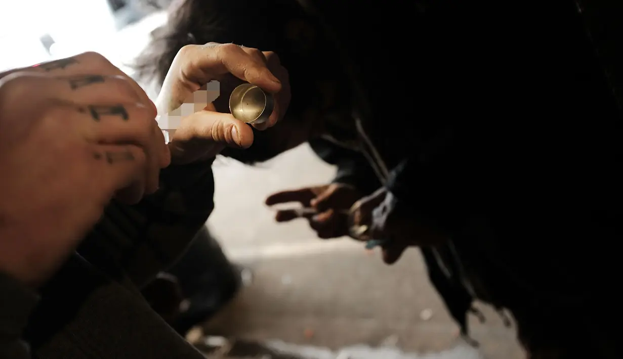 Seorang pecandu memasukan cairan ke dalam jarum suntiknya di bawah jembatan yang menjadi pusat penggunaan heroin di Kensington, Philadelphia (24/1). (Spencer Platt/Getty Images/AFP)