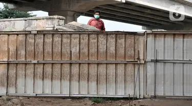 Warga berada di balik pagar pembatas yang menutup akses menuju kawasan Cipinang Melayu, Jakarta, Minggu (29/3/2020). Warga membatasi aktivitas pengunjung yang melintasi kawasan mereka dengan menutup sebagian jalan dengan seng guna mengantisipasi penyebaran corona Covid-19 (merdeka.com/Iqbal Nugroho)