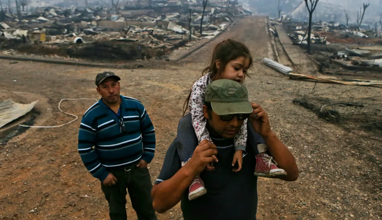 Sergio Gelvez membawa putrinya Maite Gelvez usai kebakaran yang melanda tempat tinggalnya di Santa Olga, Chile, (26/1). Sebanyak 6.000 warga berhasil menyelamatkan diri dari kebakaran hebat tersebut. (AP Photo/Esteban Felix)