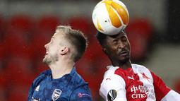 Penyerang Slavia Praha, Peter Olayinka menyundul bola melewati bek Arsenal, Rob Holding pada leg kedua perempat final Liga Europa di Stadion Sinobo, Praha, Jumat (16/4) dini hari WIB.  Arsenal lolos ke semifinal Liga Europa setelah menang telak 4-0 di markas Slavia Praha. (AP Photo/Petr David Josek)