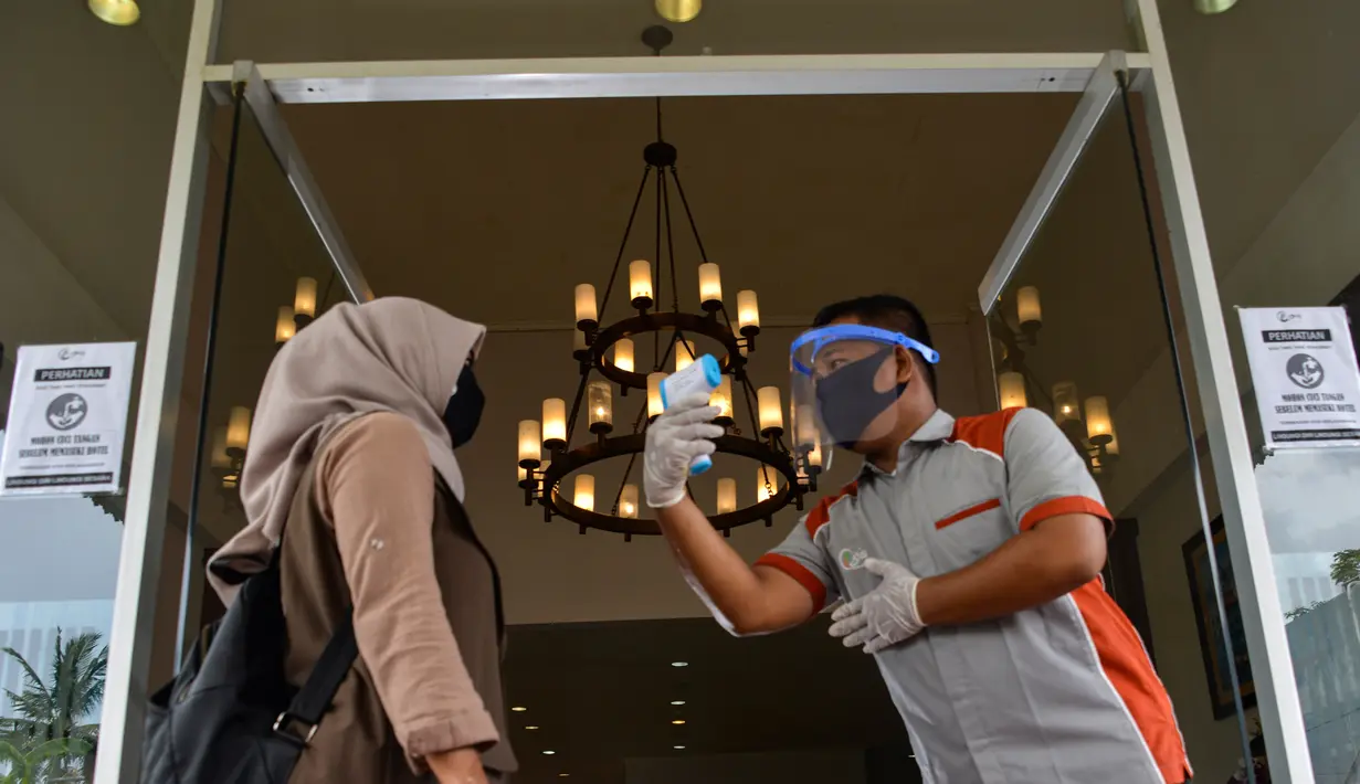 Seorang pekerja dengan mengenakan alat pelindung mengukur suhu tubuh tamu sebelum memasuki sebuah hotel yang dibuka kembali setelah ditutup selama tiga bulan akibat pandemi COVID-19 di Banda Aceh pada Rabu (15/7/2020). (Photo by CHAIDEER MAHYUDDIN / AFP)