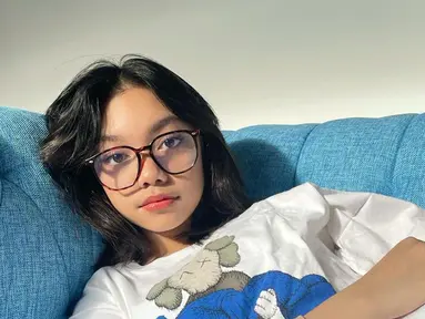 Naura berpose santai di sofa dengan kaos simple berwarna putih. Penyanyi kelahiran 2005 ini semakin memancarkan pesonanya lewat penampilannya di dunia hiburan. (Instagram/@naura.ayu)