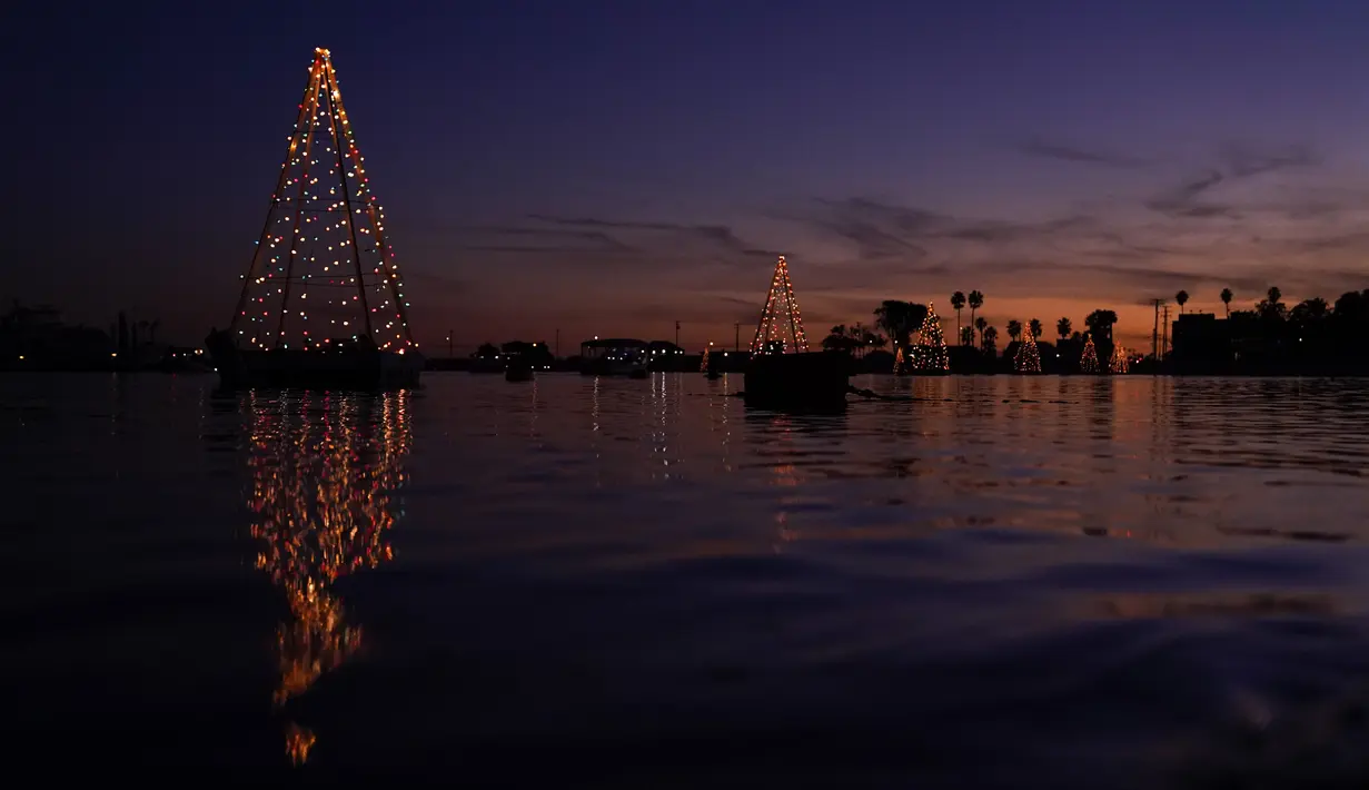 Sebuah pohon Natal mengambang yang terbuat dari lampu memantul di air di Long Beach, California, Minggu (19/12/2021). Sambut Natal, pantai di California menghiasi pantainya dengan hiasan lampu pohon Natal. (AP Photo/Ashley Landis)