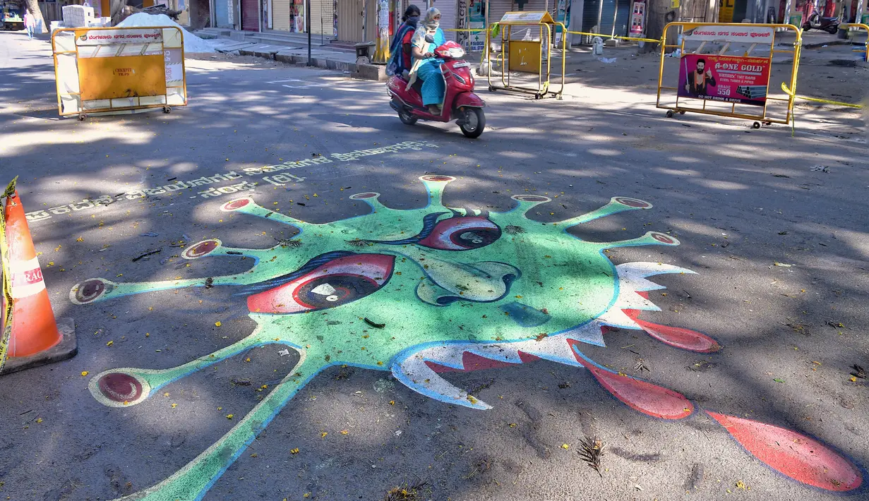 Pengendara motor melintas disamping grafiti virus  corona di persimpangan lalu lintas  di Bangalore (1/4/2020). Grafiti tersebut dibuat untuk meningkatkan kesadaran masyarakat agar mematuhi lockdown yang diberlakukan pemerintah India  sebagai langkah pencegahan COVID-19.  (AFP/Manjunath Kiran)