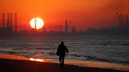 Seorang pria berjalan di dekat Industri pelabuhan Dunkirk saat matahari terbenam di Leffrinckoucke, Prancis (25/2). (Reuters/Pascal Rossignol)