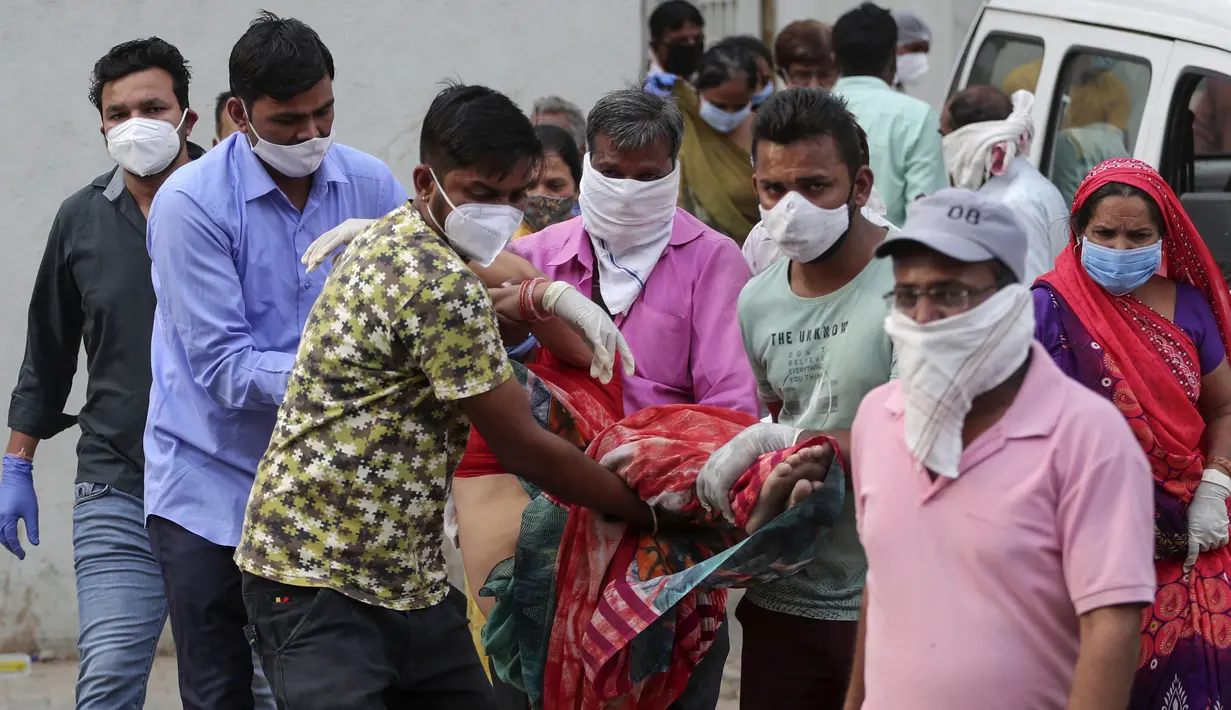 Kerabat membawa seorang perempuan yang pingsan setelah melihat tubuh suaminya di rumah sakit pemerintah khusus COVID-19 di Ahmedabad, India, Selasa (27/4/2021). Kasus virus corona di India melonjak lebih cepat dari tempat lain di dunia. (AP Photo/Ajit Solanki)