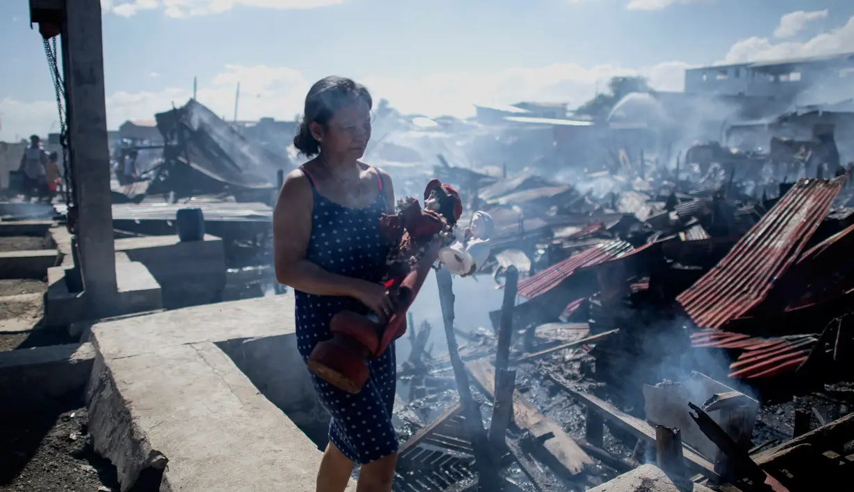 Seorang wanita berjalan membawa boneka miliknya saat rumah-rumah mereka hangus terbakar di sebuah daerah kumuh di Navotas, Manila (8/11). Dilaporkan sekitar 150 keluarga terkena dampak kebakaran tersebut. (AFP Photo/Noel Celis)