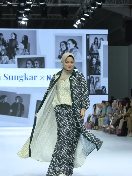 Titi Kamal memadukan outer panjang two tone yang unik. Satu sisi outer tersebut berwarna hijau lime yang senada dengan inner-nya. Sisi lainnya yang didominasi warna navy-hijau emerald selaras dengan celana panjang yang ia kenakan. [Dok/Fimela/Adrian Utama P].